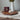 White vase with greanary against gray background displayed on a stand a medallion of Jesus Christ, based on Angela Johnson's work Because of Love.