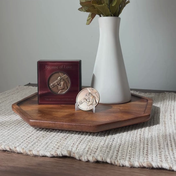 White vase with greanary against gray background displayed on a stand a medallion of Jesus Christ, based on Angela Johnson's work Because of Love.